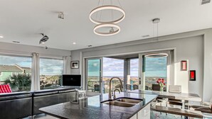 A modern kitchen with a large island, a dining area, and a view of the beach.