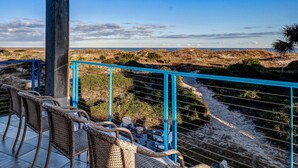 A balcony with wicker furniture overlooking a beach and dunes.