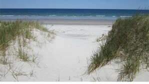 En strand med sand och gräs i förgrunden, som sträcker sig fram till havet.