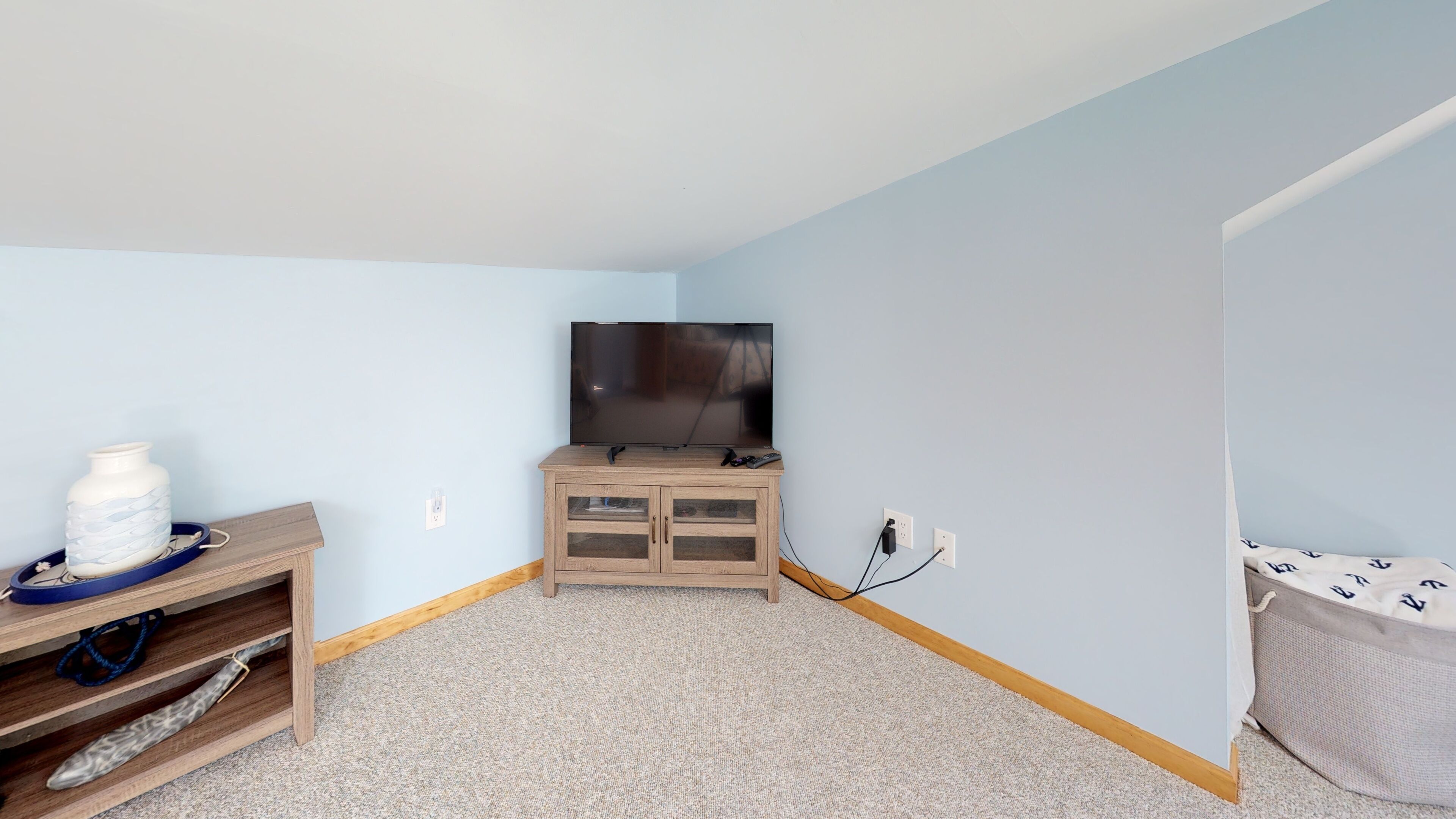A room with a TV on a wooden cabinet, a small shelf with decorative items, and a plain carpet.
