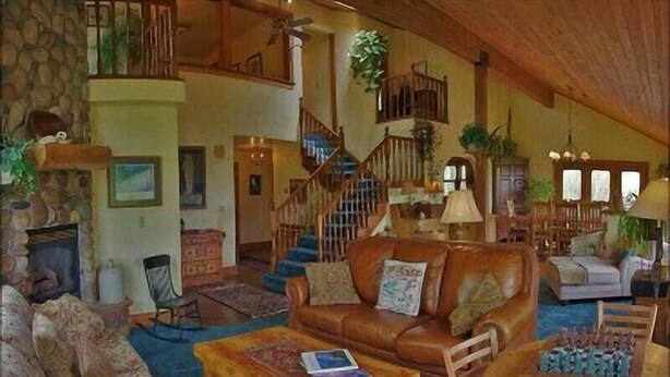A spacious living room with a stone fireplace, a wooden staircase, and a cozy seating area with a brown leather sofa and patterned armchairs. - Private Home with Great Views & Hot Tub (Steamboat Springs)