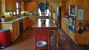 A wooden cabin-style kitchen with a central island, wooden cabinets, a stove, and a refrigerator. - Private Home with Great Views & Hot Tub (Steamboat Springs)