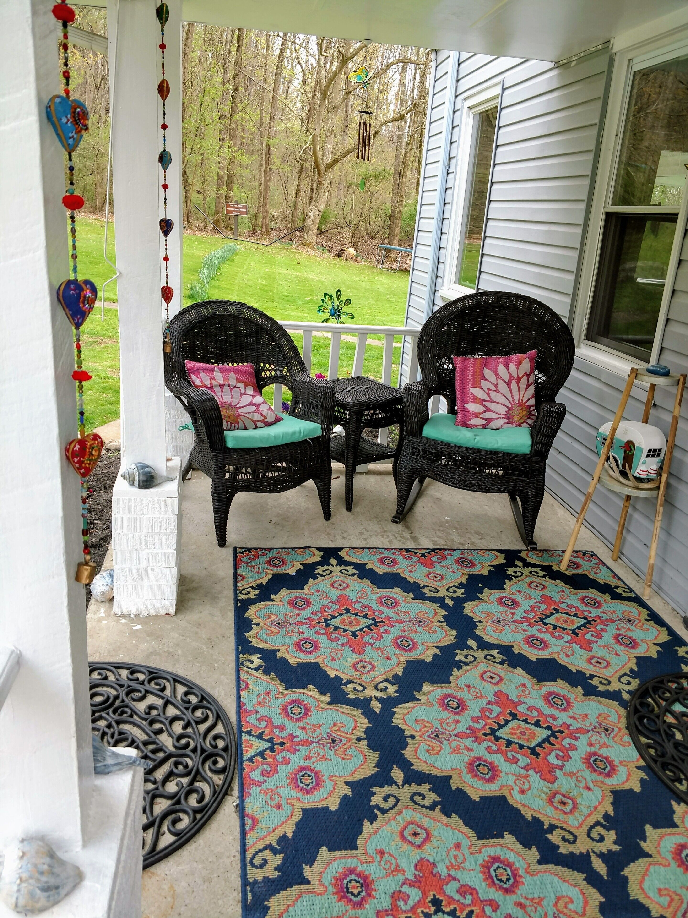 Eine Veranda mit Korbstühlen, einem gemusterten Teppich und Blick auf eine Rasenfläche.