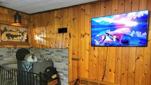 A wooden interior with a TV displaying a scenic landscape, a bench, a bear sculpture, and a welcome sign. - In the ❤ of Ohiopyle. Central location, clean, charming. Large yard with firepit (Ohiopyle)