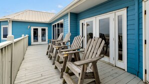 A wooden deck with Adirondack chairs, a blue building with white trim, and a white door.