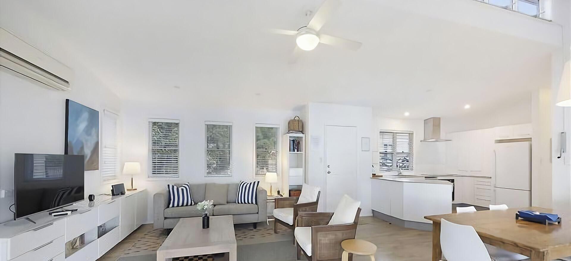 A modern living room with a flat-screen TV, sofa, coffee table, and dining area.