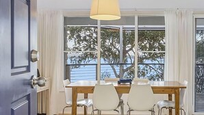Un comedor con una mesa y sillas, una ventana con vistas a árboles, y una puerta con manija.