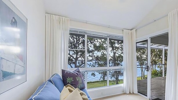 Una habitación con un ventanal grande, un sofá azul y vistas a árboles y un edificio.