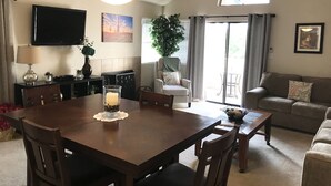 Un comedor con una mesa de madera, sillas, un ventilador de techo, un televisor y un ventanal corredizo que da a un patio.