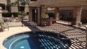 Una piscina con borde de azulejos, rodeada por una zona pavimentada con sillas y una valla.