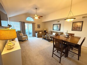 A spacious living room with a dining area, a ceiling fan, and a large window.
