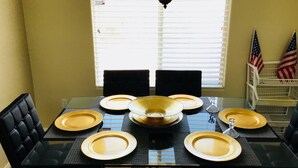 Une table à manger dressée pour six personnes, avec des chaises noires, un plateau en verre et des assiettes jaunes.