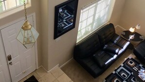Un salon avec un canapé en cuir noir, un téléviseur fixé au mur et un luminaire suspendu.