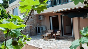 A patio area with stone flooring, a table, two chairs, and a small fan. - Villa Hera At Cape Sounion (Lavreotiki)