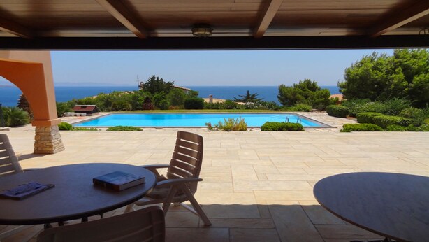 An outdoor patio with a pool, chairs, and a table. - Villa Hera At Cape Sounion (Lavreotiki)