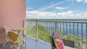 Un balcon doté de meubles en osier et offrant une vue sur un lac et une forêt.
