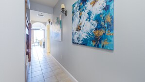 Un couloir doté d’un sol carrelé, une grande peinture abstraite sur le mur de droite et une porte au fond.