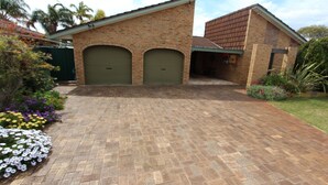 A residential property with a paved driveway, two garage doors, and a well-maintained garden with various flowers. - Seagate Beach Retreat - with private pool and integrated spa (spa is unheated). (Rockingham)