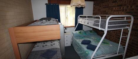 Habitación tipo dormitorio con dos literas, un escritorio de madera, una silla, un mueble bajo y una ventana con cortinas.