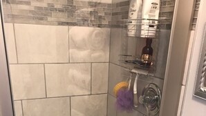 A shower with a glass door, tiled walls, and a shelf with toiletries. - Studio apartment overlooking the Snake river (Clarkston)