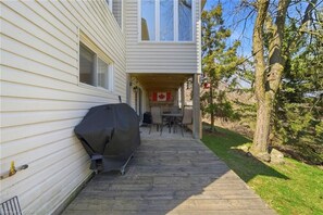 A wooden deck leading to a covered outdoor area with a table and chairs, a barbecue grill, and a Canadian flag. - River Views | Pool Table | EV Charger | Hiking Trails | Near Niagara Falls (St. Catharines)