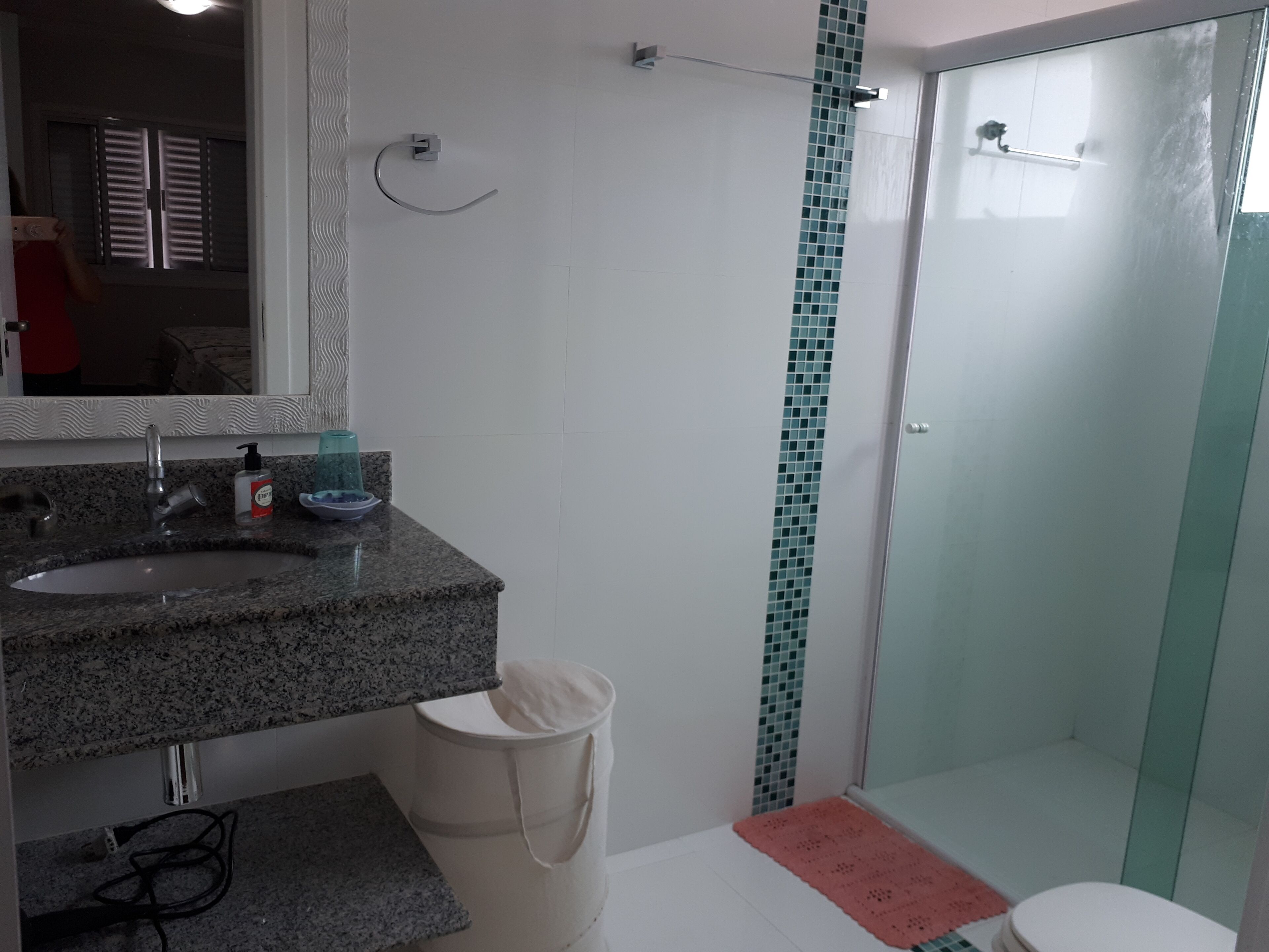 Een badkamer met een wastafel van graniet, een spiegel, een handdoekhouder, een douchecabine van glas en een toilet.