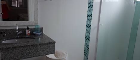 Een badkamer met een wastafel van graniet, een spiegel, een handdoekhouder, een douchecabine van glas en een toilet.