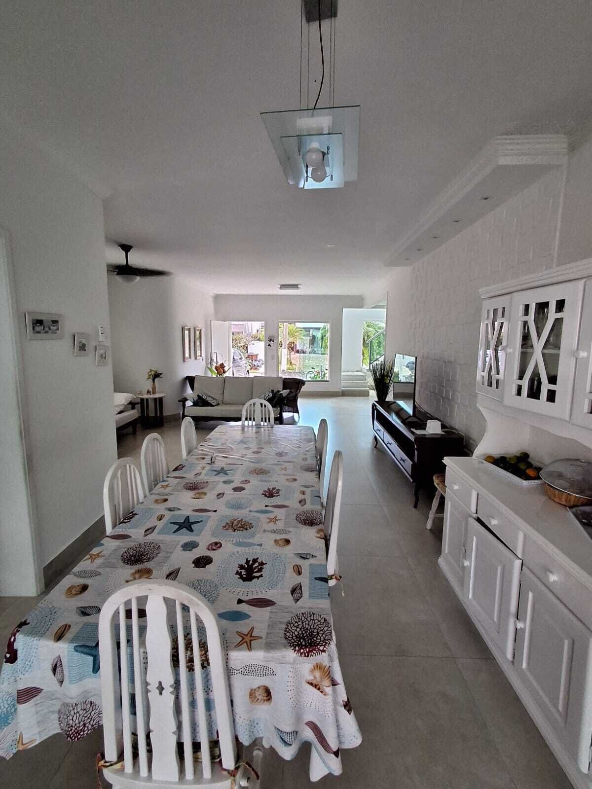 A spacious dining area with a long table, white chairs, and a ceiling fan.