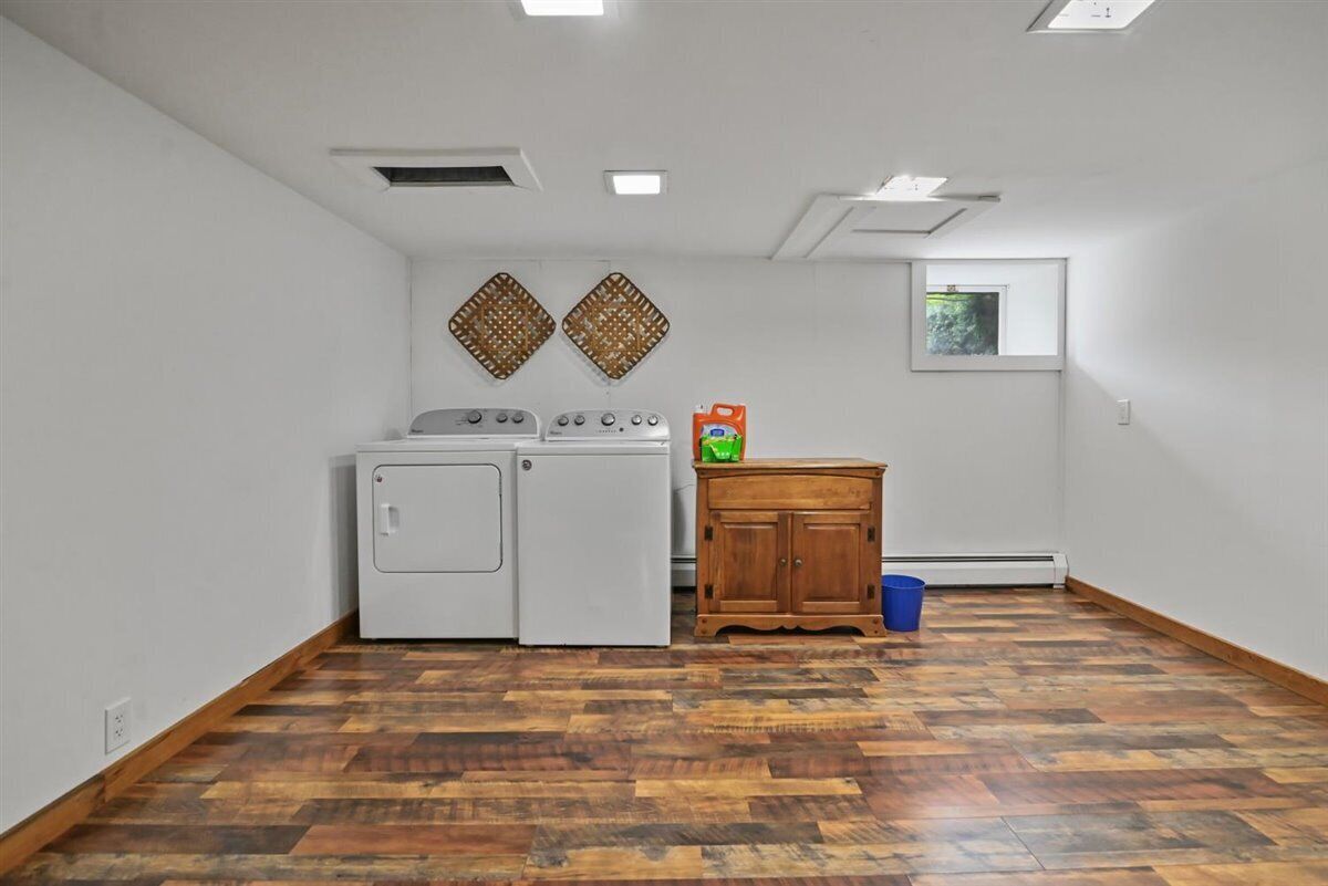 A laundry room with two washing machines, a wooden cabinet, and a window.