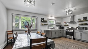 Eine moderne Küche mit weißen Schränken, einem Esstisch mit Stühlen, einem gemusterten Teppich und Pendelleuchten.