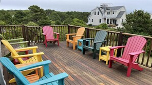 Eine Holzterrasse mit bunten Adirondack-Stühlen und einem Haus im Hintergrund.
