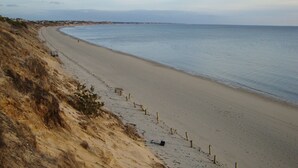 Ein Strand mit einer Holzbank entlang der Küste, feiner Sand und ein freier Blick auf den Ozean.