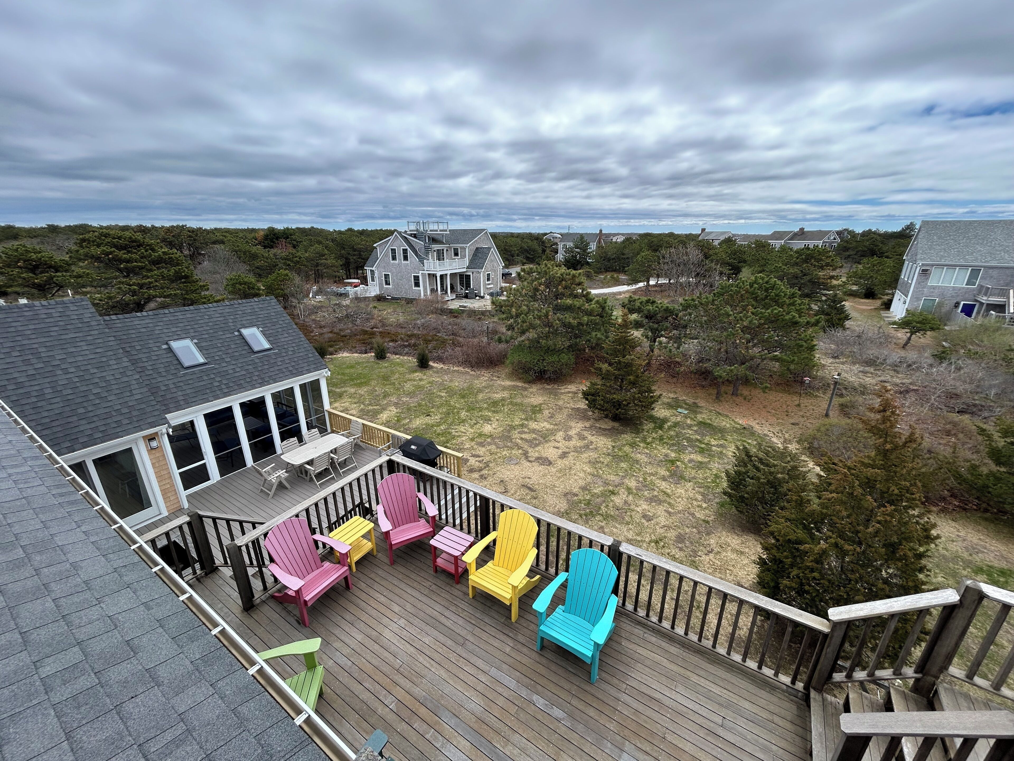 Une terrasse agrémentée de chaises Adirondack aux couleurs vives, d’un patio couvert et offrant une vue sur un quartier résidentiel.