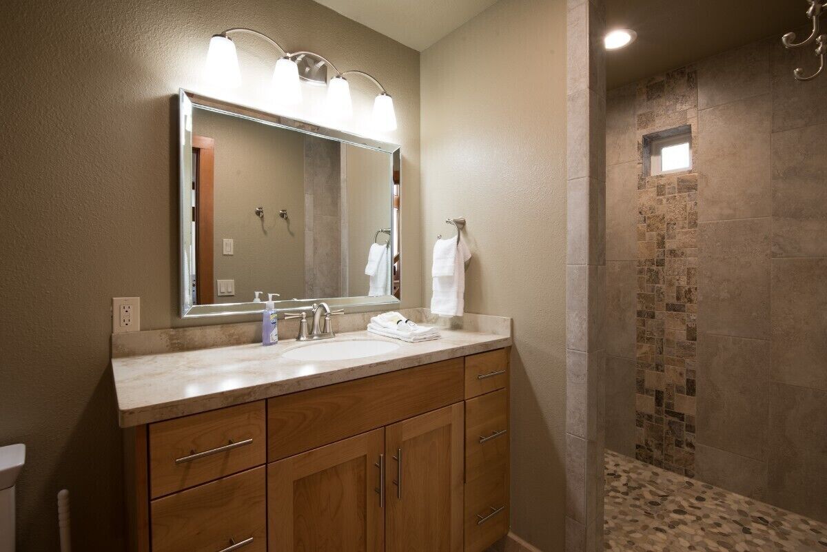Un baño con un espejo grande, un lavabo y una zona de ducha con mosaicos.