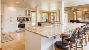A spacious kitchen with a large island, white cabinetry, and a bar area with stools. - Spacious Home - Hot Tub, Game Room, 2 Kitchens, 3 Living Rooms - Perfect For Large Families (Ketchum)
