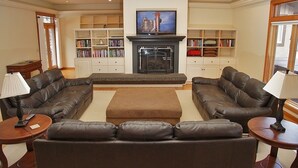 A living room with two leather sofas, a fireplace, and bookshelves. - Spacious Home - Hot Tub, Game Room, 2 Kitchens, 3 Living Rooms - Perfect For Large Families (Ketchum)