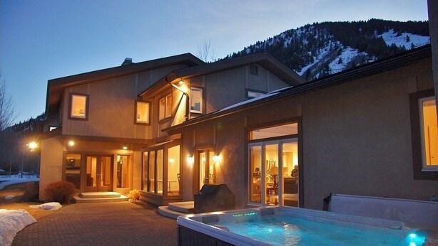 A modern two-story house with a hot tub in the backyard, surrounded by a snowy landscape and mountains in the background. - Spacious Home - Hot Tub, Game Room, 2 Kitchens, 3 Living Rooms - Perfect For Large Families (Ketchum)