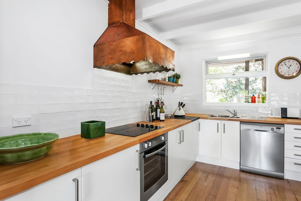 A modern kitchen with white cabinetry, a wooden countertop, a stainless steel dishwasher, and a copper range hood.
