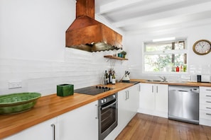 A modern kitchen with white cabinetry, a wooden countertop, a stainless steel dishwasher, and a copper range hood.