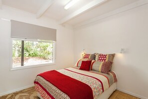 A bedroom with a large window, a bed with patterned bedding, and a view of greenery outside.