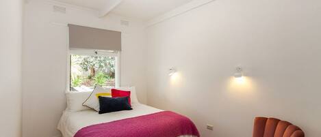Ein Schlafzimmer mit einem Bett, einem Fenster, einem Sessel und einer Lampe.