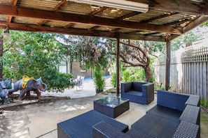 An outdoor patio with wicker furniture, a glass-top table, and a decorative elephant sculpture.
