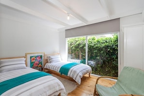 A bedroom with two beds, a large window, and a view of greenery.