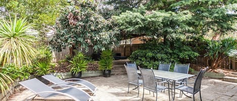 An outdoor patio area with a table and chairs, surrounded by potted plants and trees.