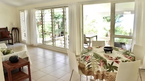 A spacious room with a large sliding glass door leading to a balcony, a dining table with chairs, and a sofa with cushions.
