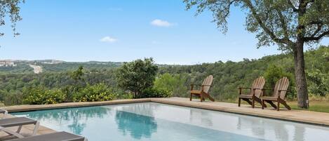 A swimming pool with lounge chairs and a view of a hilly landscape.
