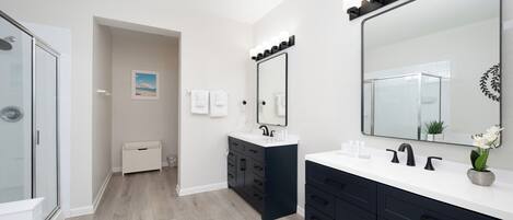 A modern bathroom with two sinks, a large mirror, and a walk-in shower.