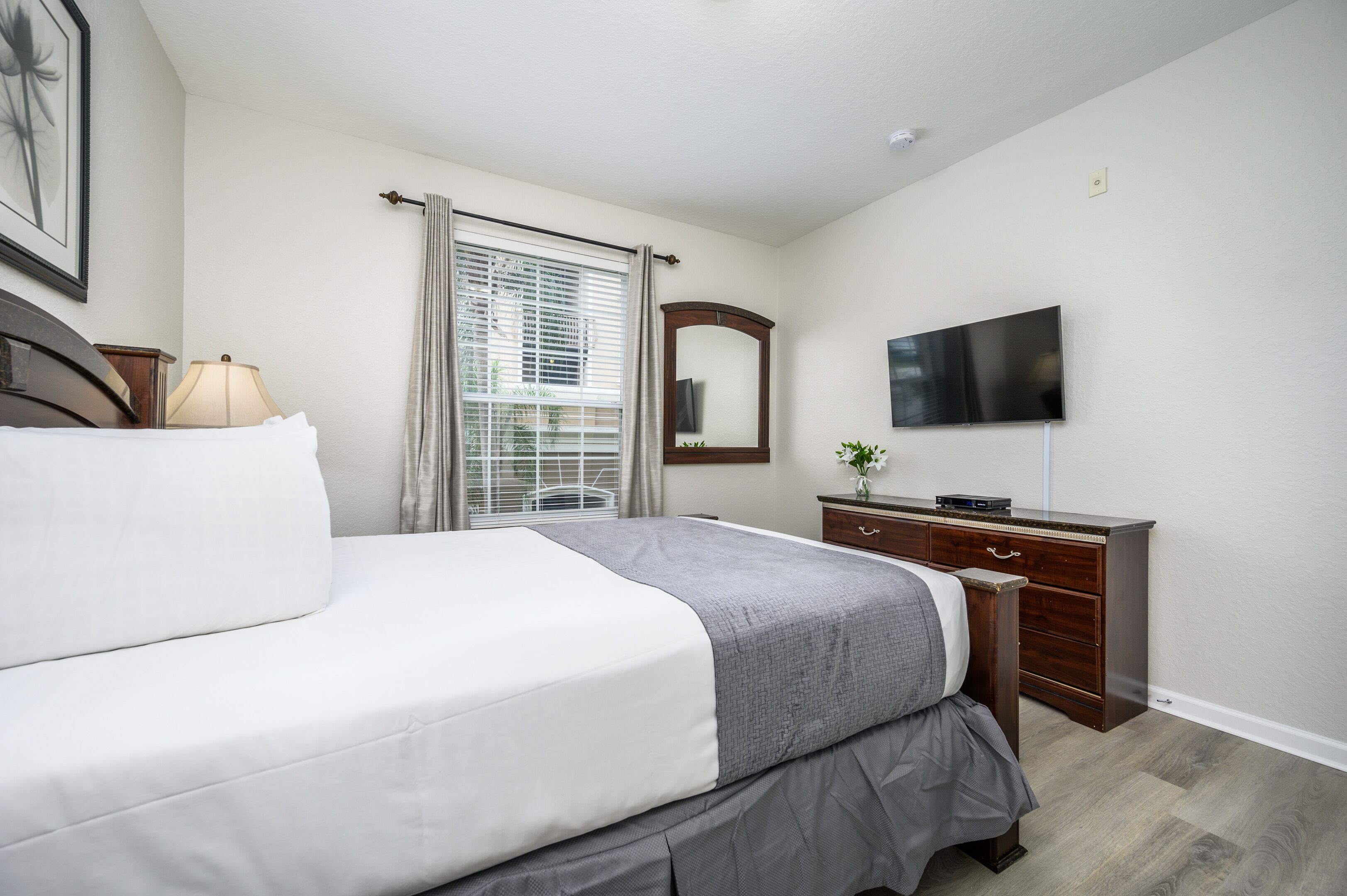 Une chambre bien rangée, avec un lit, une commode, un téléviseur et une fenêtre avec des rideaux.