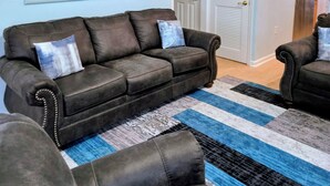 Een woonkamer met een donkerbruine leren bank, een blauw-wit gestreept tapijt, en een groot schilderij met een zeelandschap.