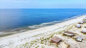 A coastal area with a sandy beach and several buildings with flat roofs, likely residential or small commercial structures. - Blessed at the Beach - Gulf View, Heated Pool and Jacuzzi. (Dauphin Island)